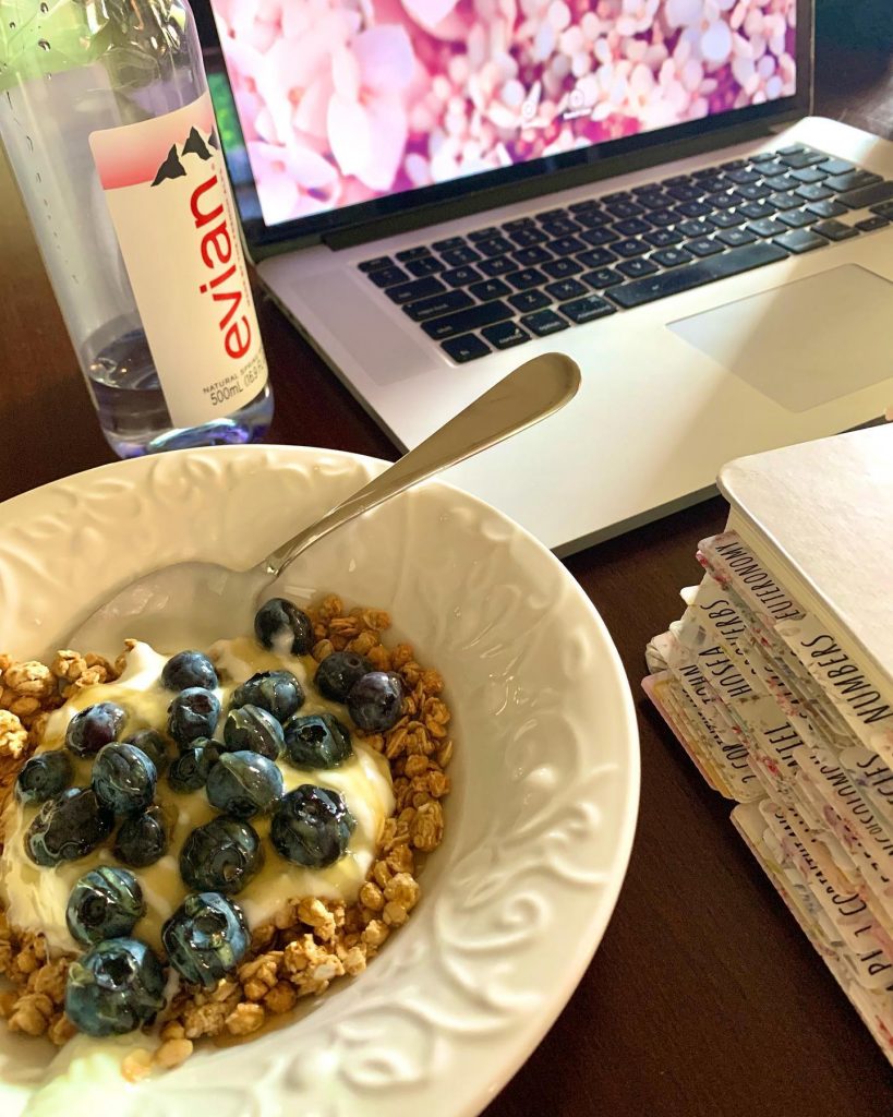 An elegantly set breakfast table featuring a fine china bowl filled with oatmeal, a bottle of water, and a charming Bible beside a modern laptop. Sunlight streams in, casting a warm glow over the scene.